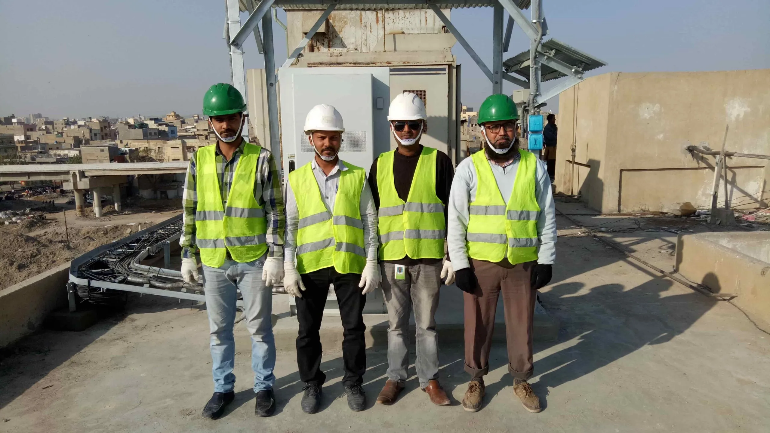 Four field team members wearing safety helmets and high-visibility vests at a rooftop infrastructure site